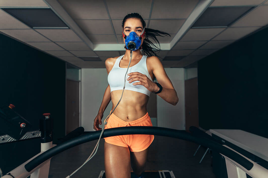 A woman running on a treadmill with a mask on to calculate her VO2 Max