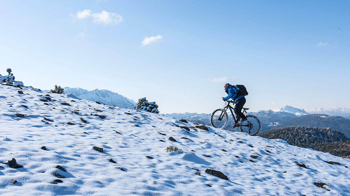 A cyclist biking up a trail in the winter with snow on the ground
