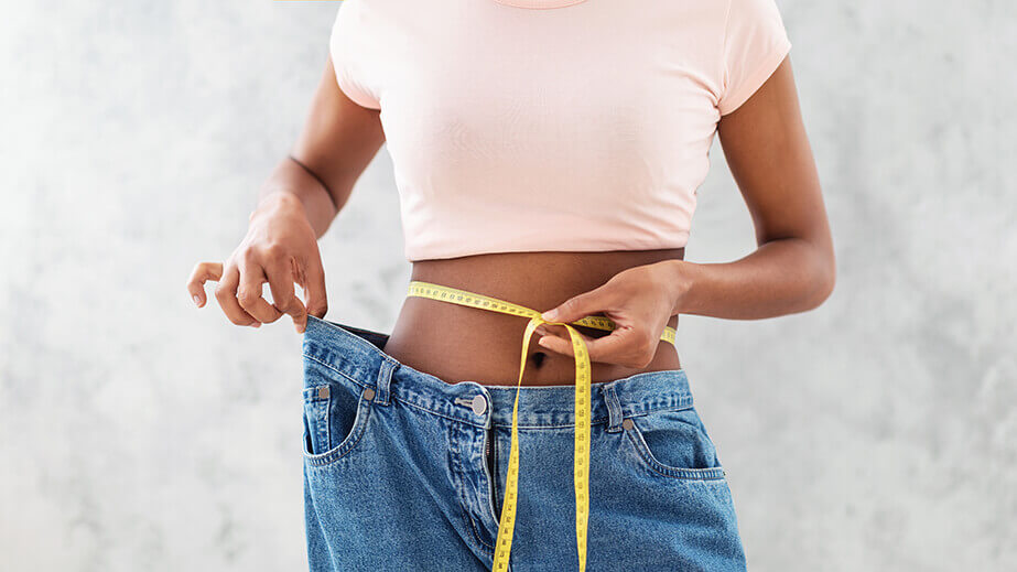 A woman in oversized jeans showing the belly fat loss from working out and good nutrition