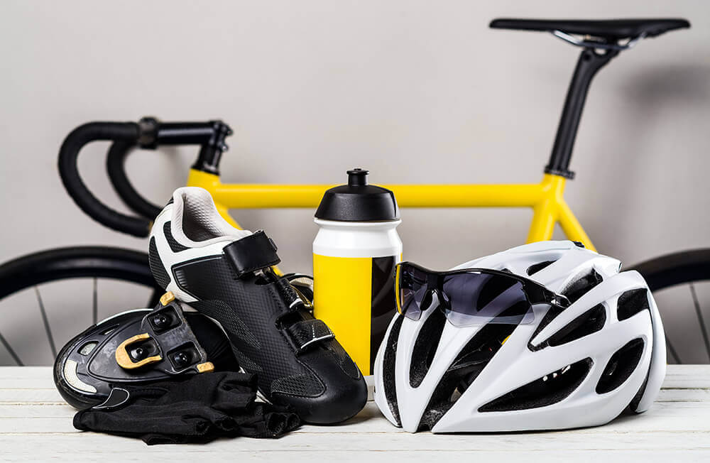 Cycling accessories including a hemet, water bottle, shoes, and a bicycle in the background
